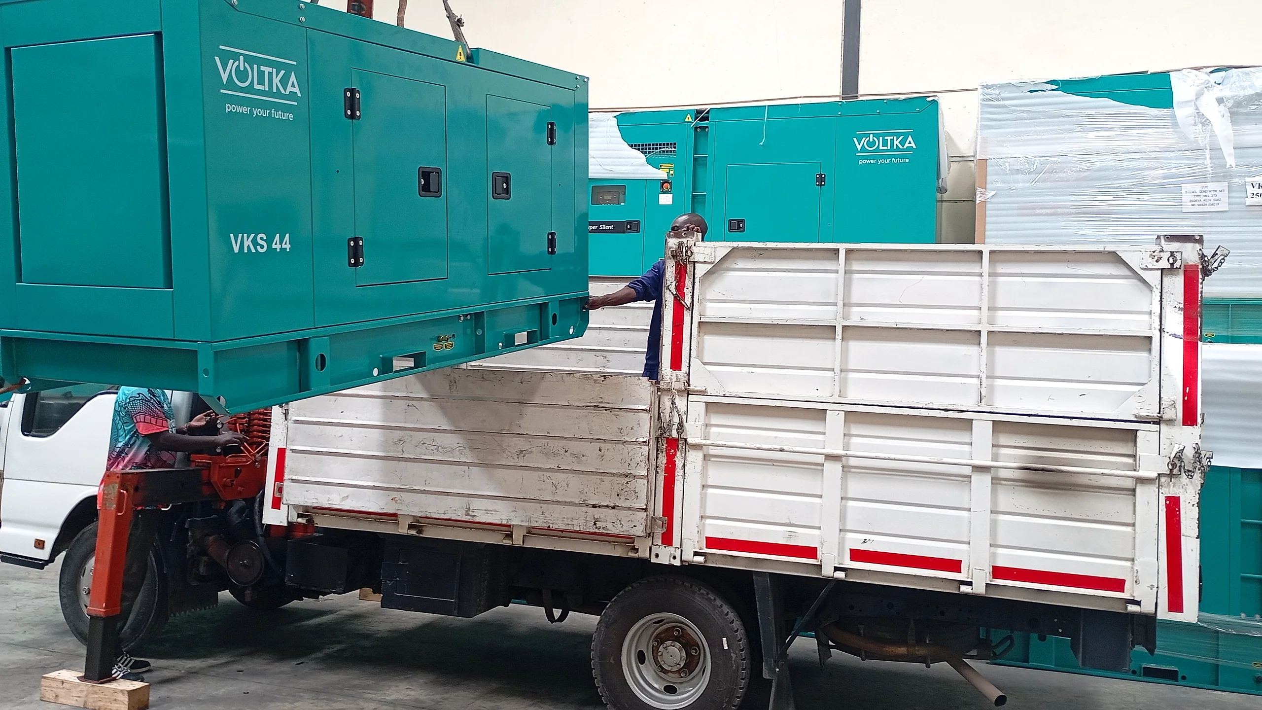 VOLTKA VKS 44 generator lifted by crane above a delivery truck, front angle showing VOLTKA branding